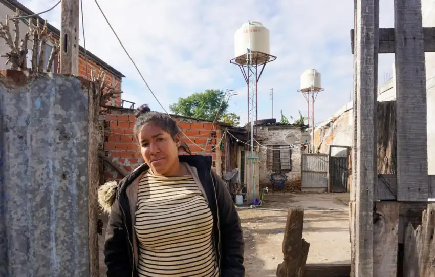 Josefina Tamara Villalba posa para una fotografía en la puerta de su casa en el barrio popular El Tambo. En el fondo, se ven los tanques de agua instalados con financiación del Fondo de Integración Socio Urbana. Lucila Pellettieri, GPJ Argentina